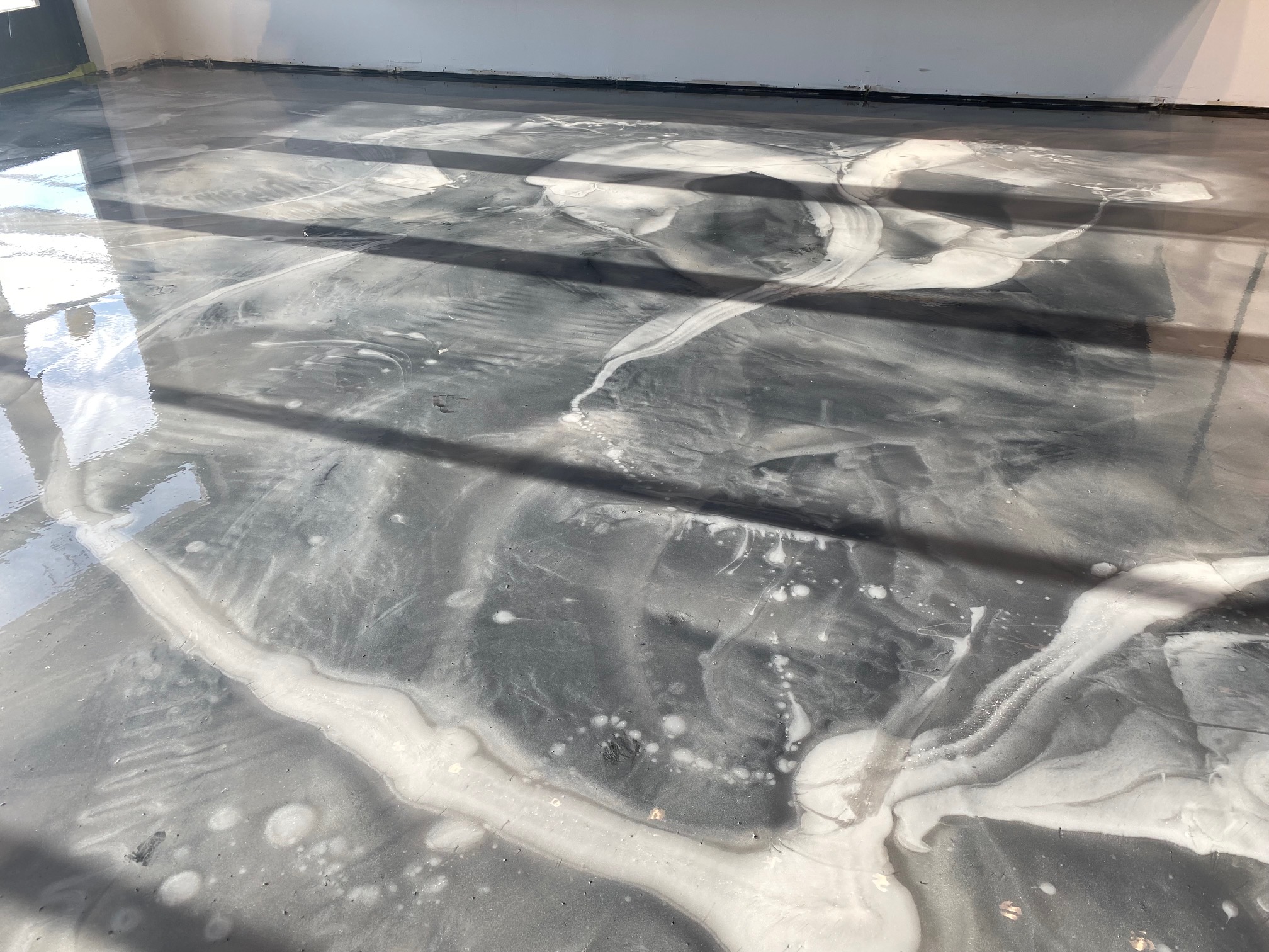 Sunlight casting window shadows across a glossy black-and-white metallic epoxy floor